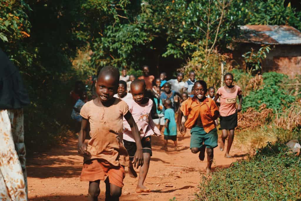 A group of girls running towards us on a dirt path on a sunny day in Tanzania