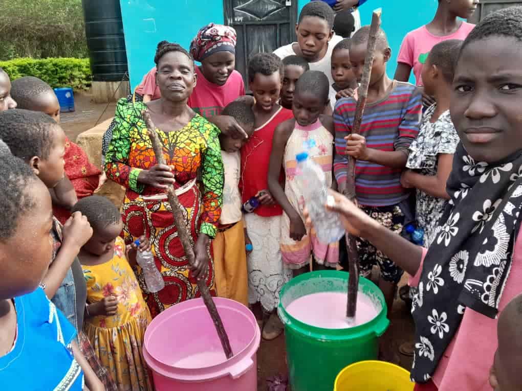girls and women dressed in colourful clothes stirring food in plastic pots